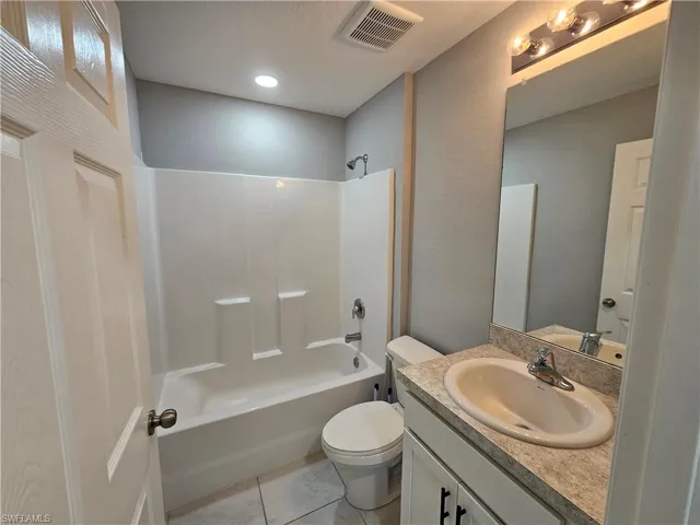 Bathroom featuring a white tub and shower combination, a single vanity with an integrated sink, a large wall-mounted mirror, and tile flooring
