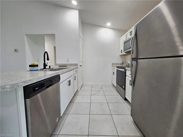 Galley kitchen featuring stainless steel appliances, white cabinetry with matte black hardware, light-toned countertops, and recessed lighting