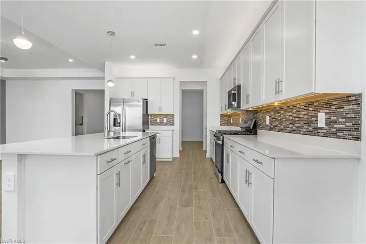 Upgraded kitchen featuring custom glass tile backsplash, pendant lighting, custom shelving in walk-in pantry, Over cabinet and under cabinet lighting, and additional recessed lights making this home bright and airy.