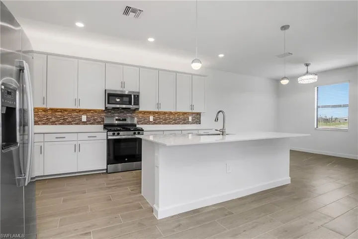 Open Kitchen/Dining space featuring glass tile backsplash, designer pendant lighting, and overhead light which also converts to a ceiling fan.