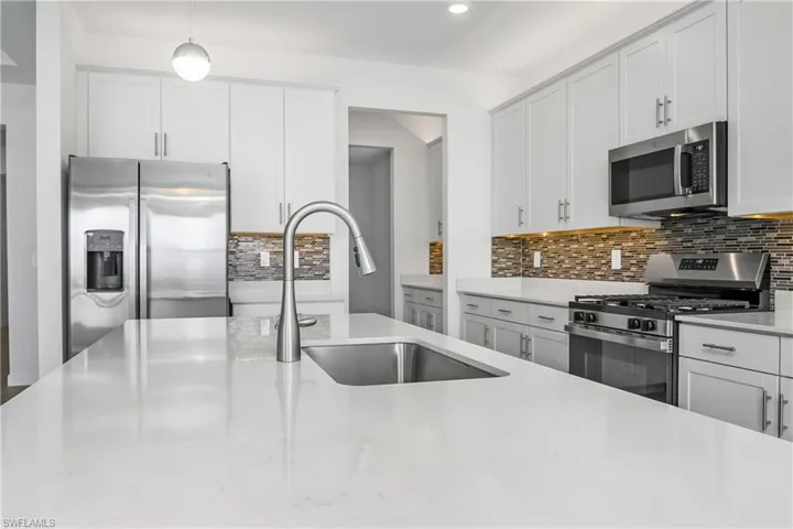 Kitchen featuring sink, light hardwood / wood-style floors, pendant lighting, white cabinets, and appliances with stainless steel finishes
