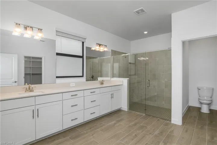 Owner bath features an oversized vanity with dual sinks, a huge walk-in shower with frameless glass enclosure, and a window with privacy film allowing plenty of natural light.