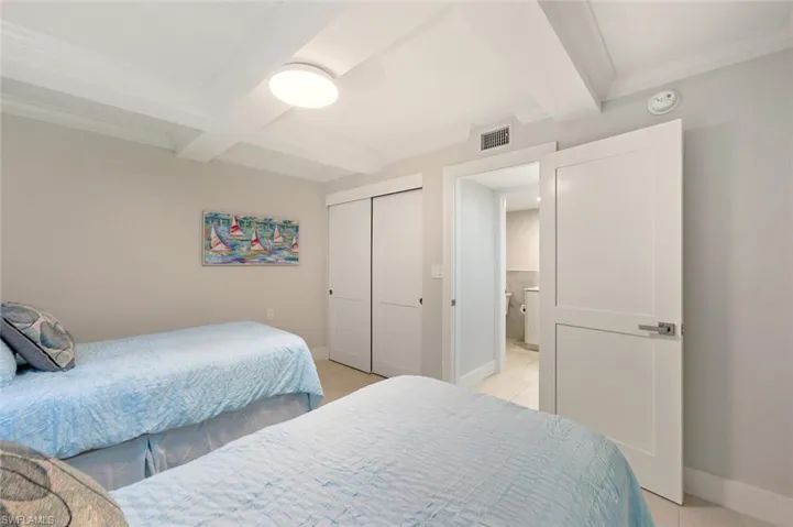 Bedroom featuring a closet, coffered ceiling, crown molding, and light tile patterned floors