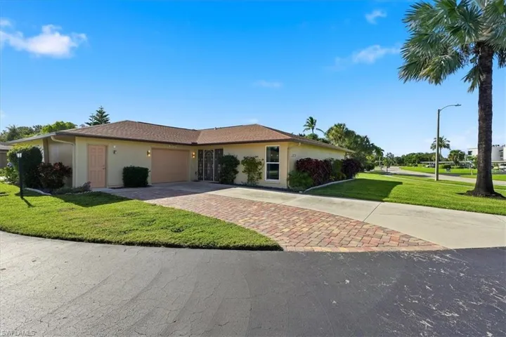 Single-story residence featuring a multi-toned paver driveway, attached garage, shingled hip roof, and exterior landscaping