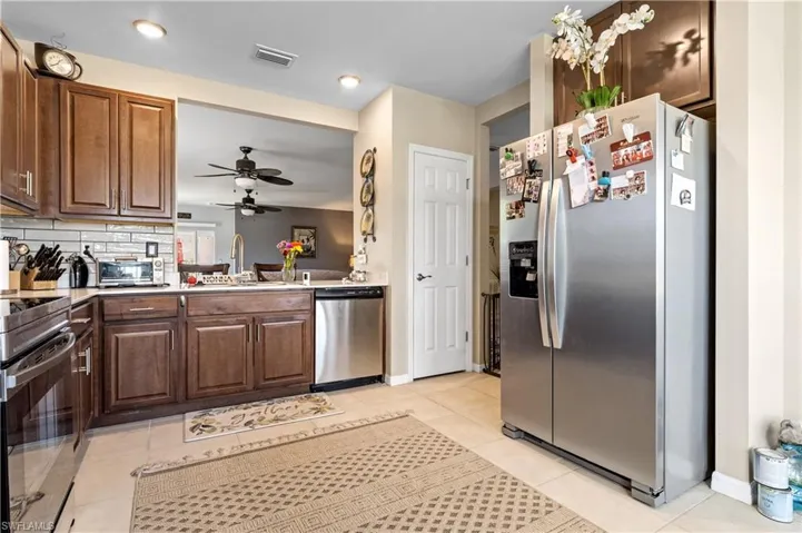 Kitchen with appliances with stainless steel finishes, a sink, a ceiling fan, light tile patterned floors, and light countertops