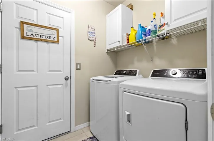 Washroom featuring cabinet space, independent washer and dryer, light tile patterned floors, and baseboards
