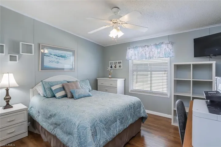 Guest bedroom features wood-look flooring, ceiling fan with light fixture, window with blinds, and vaulted ceiling.