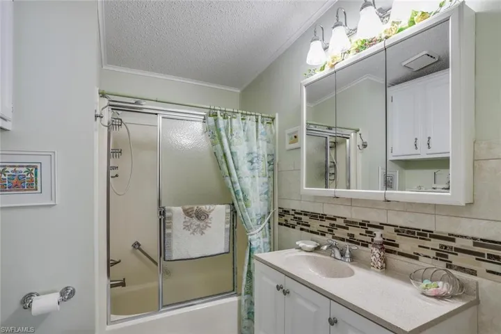 Guest bathroom features vanity with quartz counter an integrated sink, polished chrome faucet, and a tiled backsplash featuring decorative mosaic accents.