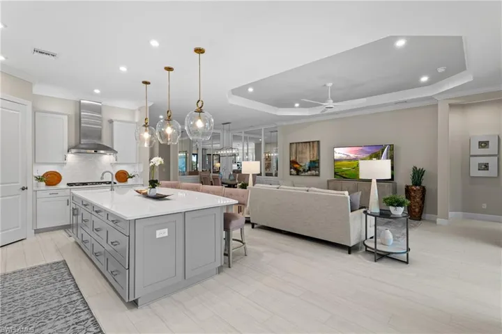 Kitchen featuring a center island with sink, gray cabinets, backsplash, wall chimney range hood, and a raised ceiling