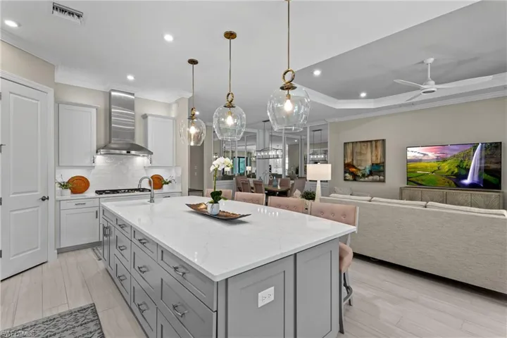Kitchen featuring visible vents, gray cabinetry, crown molding, and wall chimney range hood