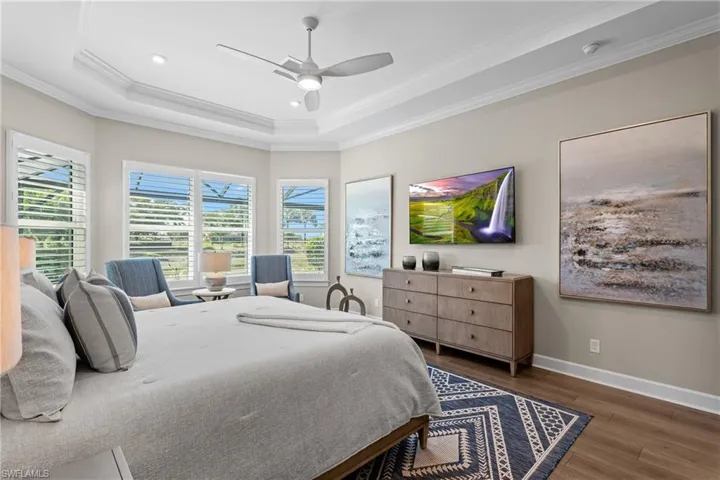Bedroom with a tray ceiling, wood finished floors, baseboards, and ornamental molding