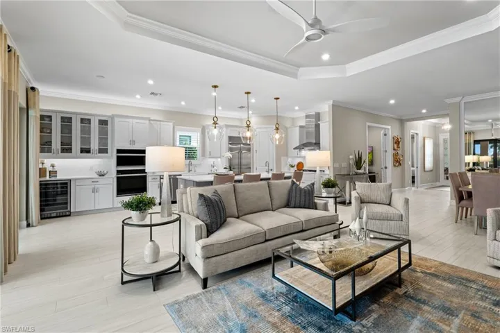 Living room with wine cooler, ornamental molding, recessed lighting, a raised ceiling, and a ceiling fan