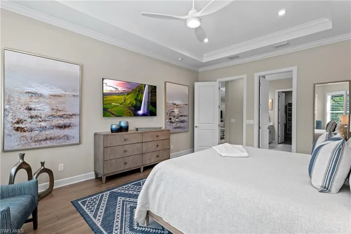 Bedroom featuring visible vents, a raised ceiling, wood finished floors, and ornamental molding