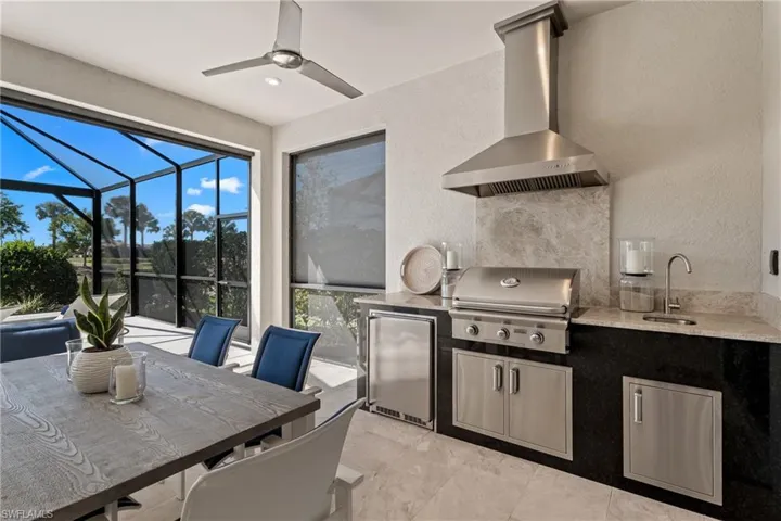 Kitchen featuring a ceiling fan, a sunroom, a sink, stainless steel refrigerator, and wall chimney exhaust hood