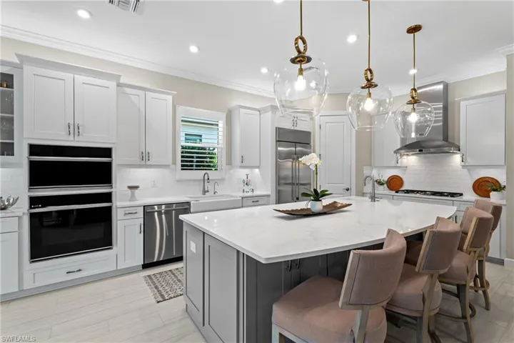 Kitchen featuring a kitchen island with sink, a sink, stainless steel appliances, wall chimney exhaust hood, and crown molding
