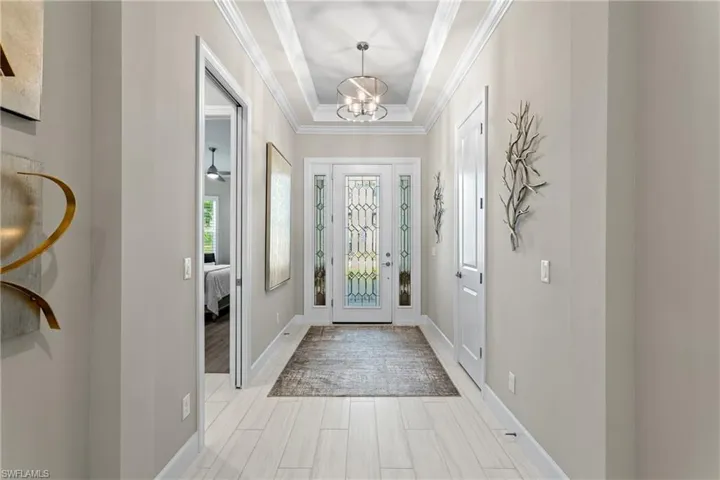 Entryway with light wood-style flooring, ornamental molding, baseboards, and a chandelier