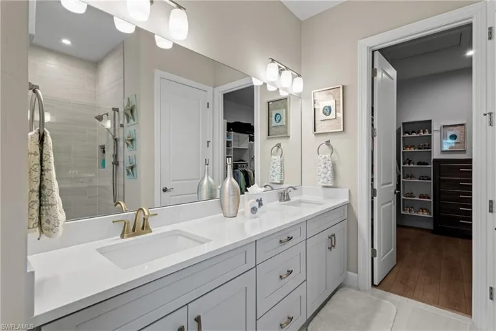 Full bath with double vanity, a spacious closet, a tile shower, and a sink