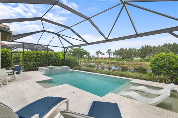 View of pool with a patio area, a water view, a pool with connected hot tub, and glass enclosure