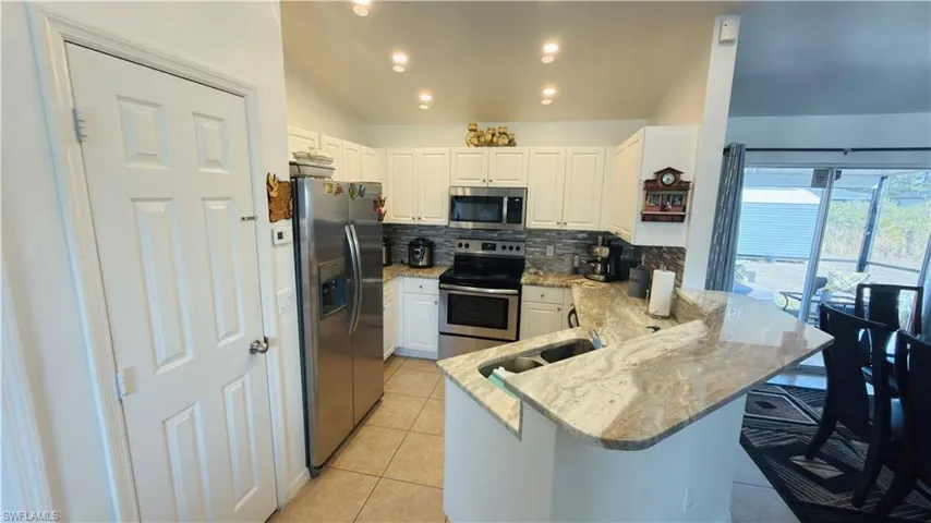 Kitchen with stainless steel appliances, a peninsula, white cabinets, light stone countertops, and backsplash