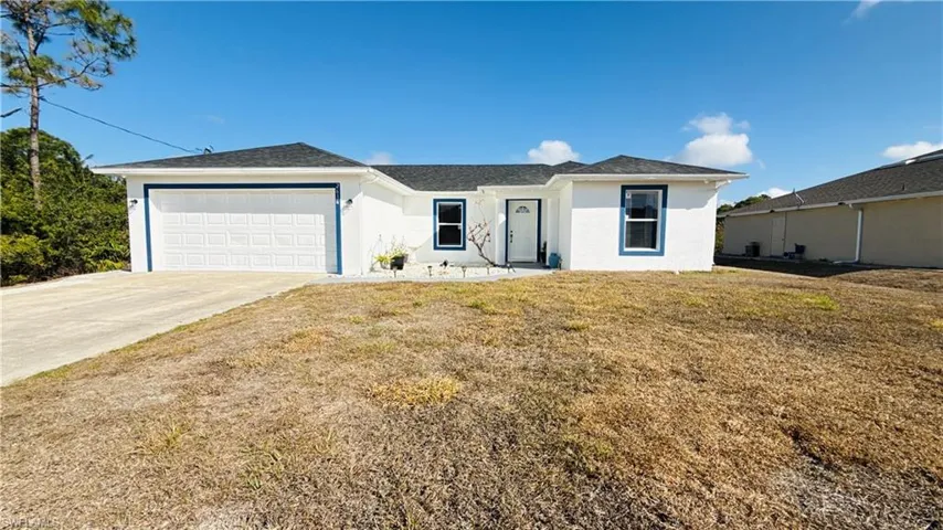 Front of the property featuring a garage, driveway, a front lawn, stucco siding, and a shingled roof