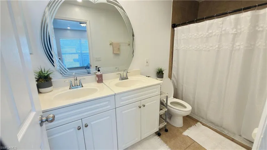 Full bathroom featuring double vanity, a shower with curtain, and light tile patterned flooring