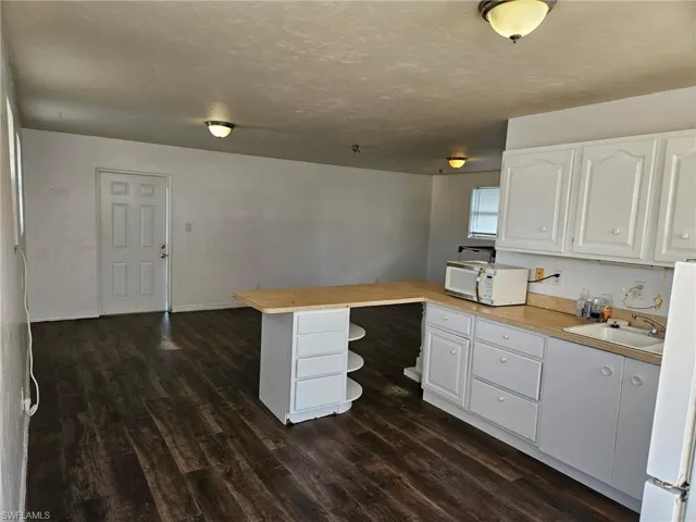 Kitchen with a peninsula, light countertops, white cabinets, white appliances, and a textured ceiling