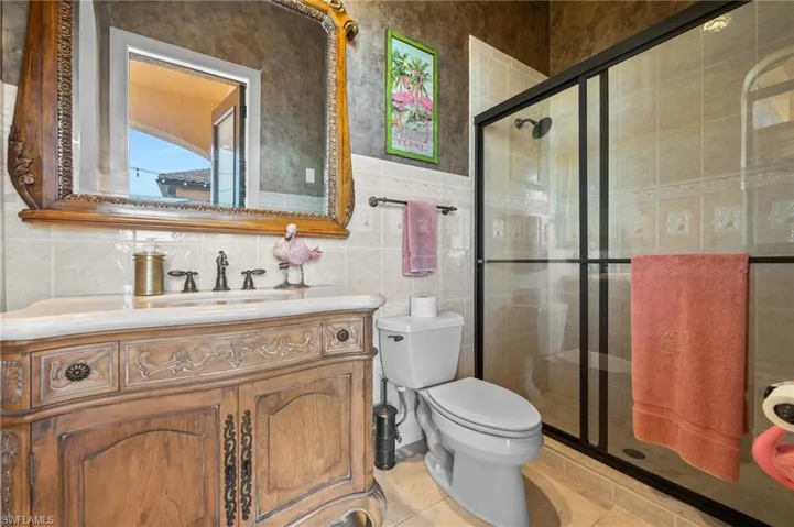 Bathroom featuring tile patterned flooring, toilet, tile walls, an enclosed shower, and vanity