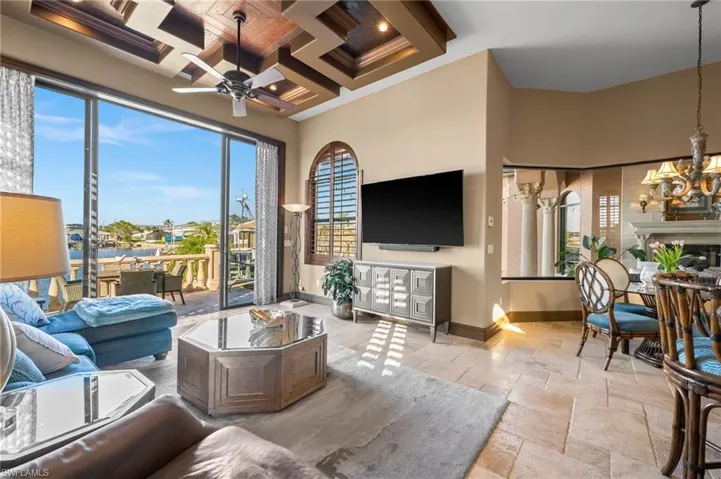 Living room with coffered ceiling, beamed ceiling, and ceiling fan with notable chandelier