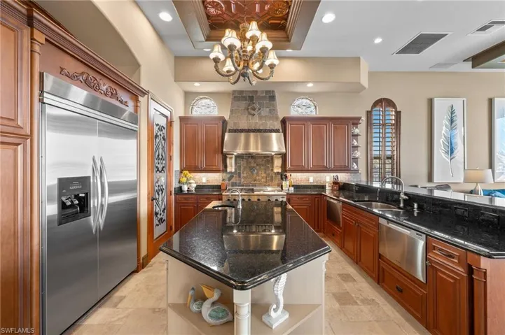 Kitchen with kitchen peninsula, a kitchen island with sink, built in fridge, a tray ceiling, and dark stone counters