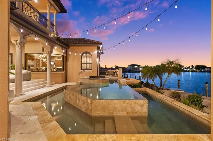 Pool at dusk with a patio, a water view, and an in ground hot tub