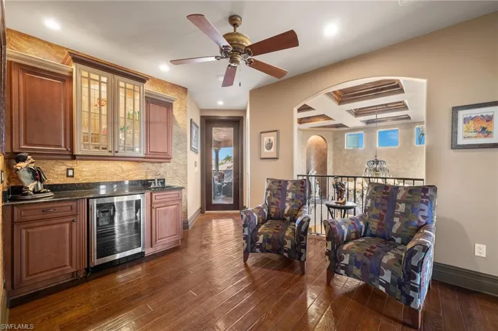 Bar featuring dark stone countertops, coffered ceiling, beverage cooler, beamed ceiling, and dark hardwood / wood-style flooring