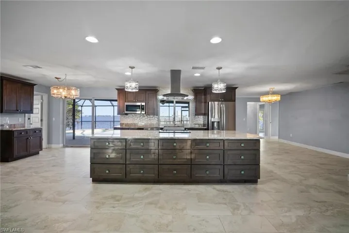 Kitchen with stainless steel appliances, hanging light fixtures, exhaust hood, and a notable chandelier