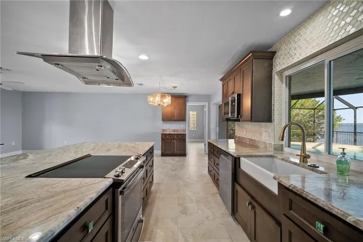 Kitchen featuring decorative light fixtures, sink, island exhaust hood, stainless steel appliances, and light stone countertops