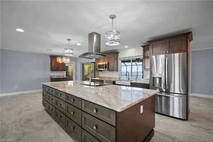 Kitchen featuring sink, appliances with stainless steel finishes, island exhaust hood, a kitchen island, and decorative light fixtures