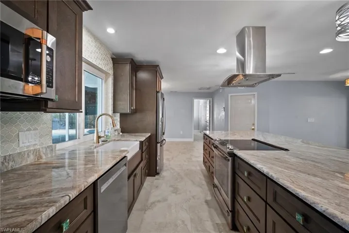 Kitchen with light stone counters, sink, island range hood, and appliances with stainless steel finishes