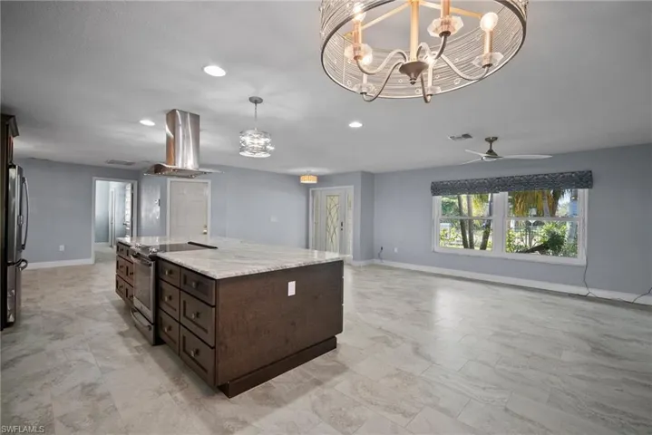 Kitchen with appliances with stainless steel finishes, island exhaust hood, light stone counters, a center island with sink, and decorative light fixtures