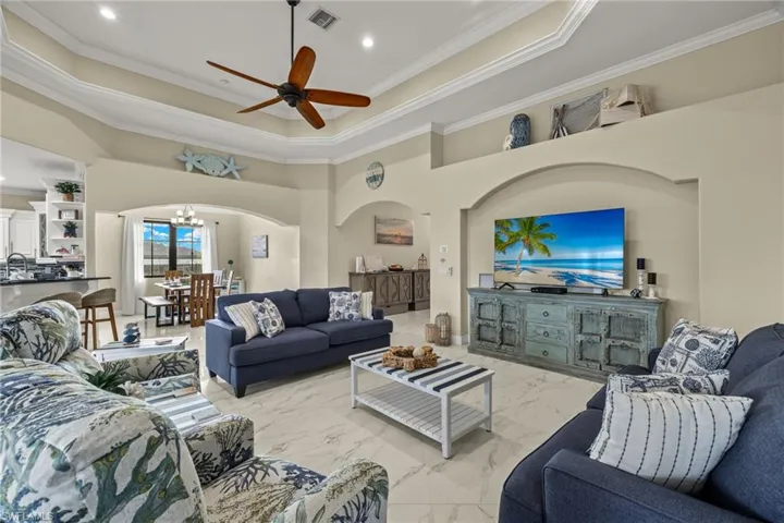 Tiled living room with ceiling fan with notable chandelier, ornamental molding, a towering ceiling, and a tray ceiling