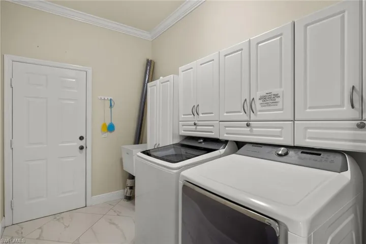 Clothes washing area featuring separate washer and dryer, crown molding, cabinets, and light tile patterned floors