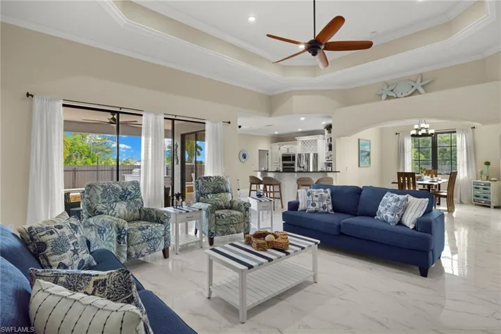 Tiled living room featuring crown molding, ceiling fan with notable chandelier, and a tray ceiling