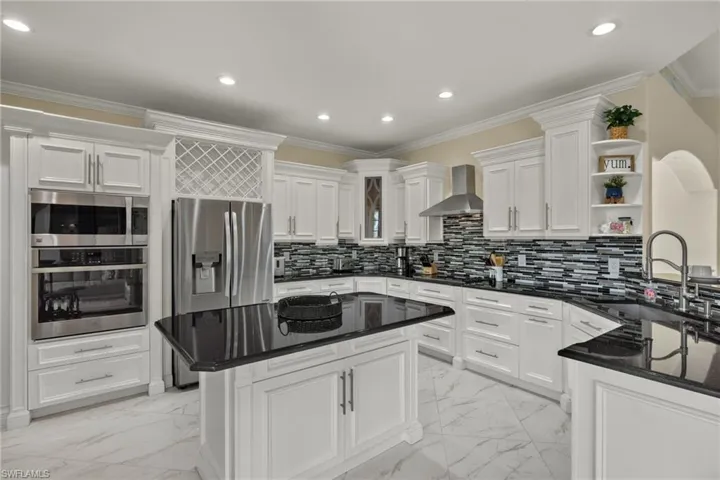 Kitchen with wall chimney exhaust hood, backsplash, a center island, white cabinets, and light tile patterned flooring