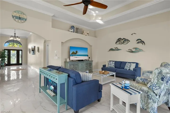 Tiled living room with ceiling fan with notable chandelier, a raised ceiling, and crown molding
