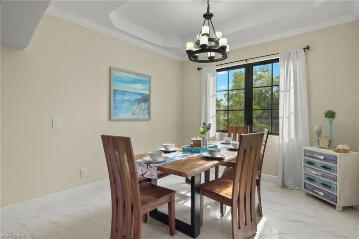 Tiled dining space with a tray ceiling, ornamental molding, and a notable chandelier