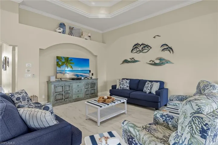 Living room featuring a raised ceiling, ornamental molding, light tile patterned floors, and a towering ceiling