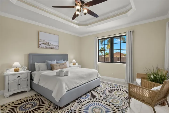 Tiled bedroom featuring a tray ceiling, crown molding, and ceiling fan