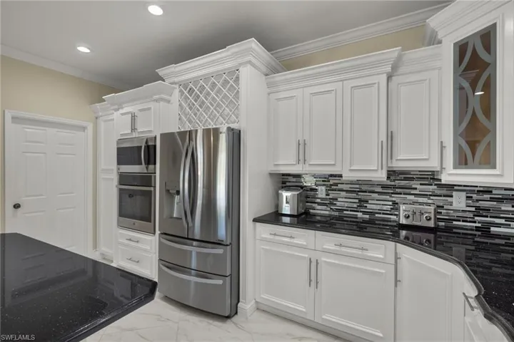Kitchen with ornamental molding, white cabinetry, tasteful backsplash, light tile patterned floors, and appliances with stainless steel finishes