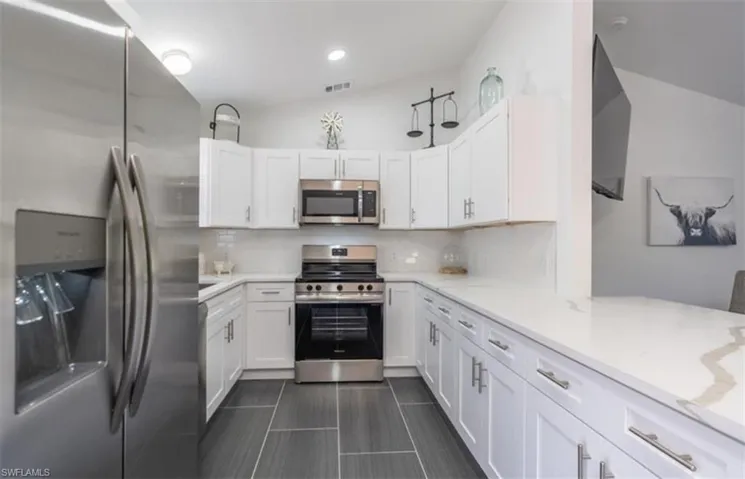 Kitchen with stainless steel appliances, white cabinets, tasteful backsplash, light stone countertops, and vaulted ceiling