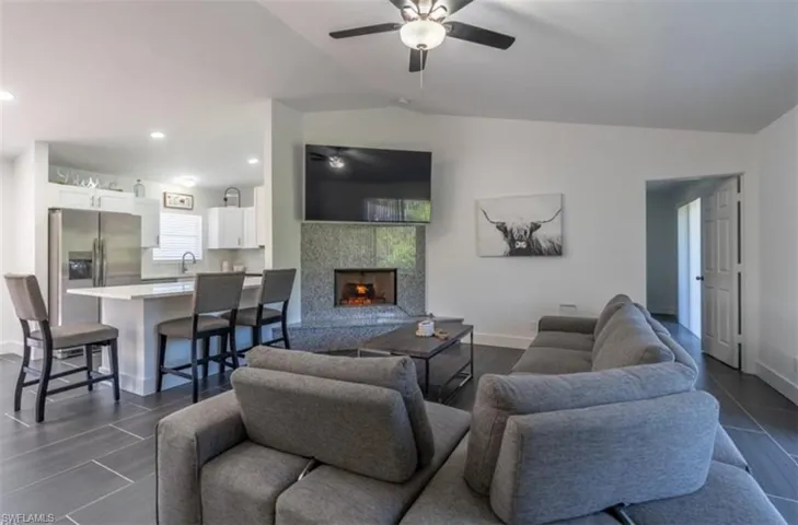Living area featuring a warm lit fireplace, a ceiling fan, lofted ceiling, wood tiled floors, and recessed lighting