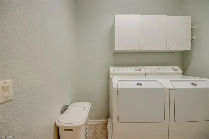 Laundry area with a textured wall, independent washer and dryer, light tile patterned floors, and cabinet space