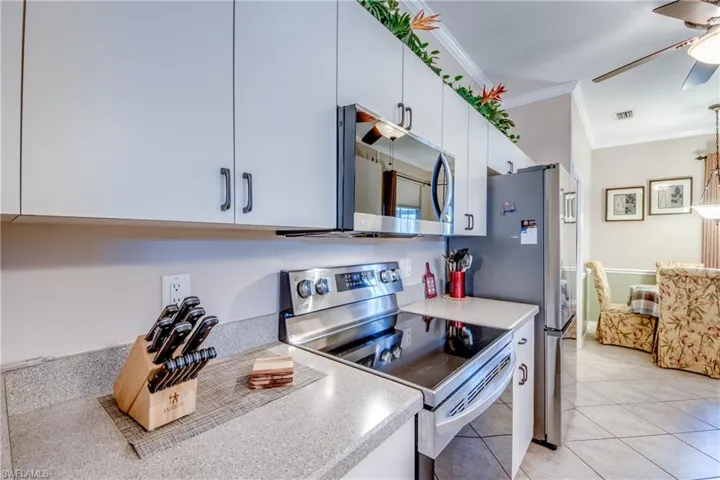 Kitchen featuring appliances with stainless steel finishes, crown molding, light tile patterned flooring, white cabinets, and ceiling fan