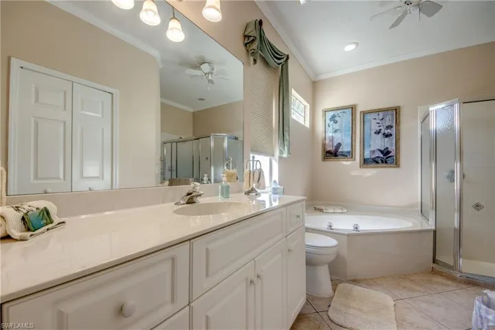 Bathroom with a ceiling fan, vanity, ornamental molding, a stall shower, and a garden tub